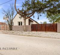 Családi ház Alistálon fallal és kapuval, fákkal és cementtel körülvéve.