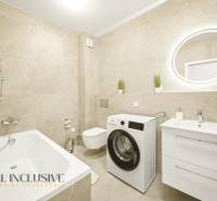 Fürdőszoba zuhanyzóval, mosógéppel és mosdóval egy négy szobás lakásban bézs csempével.