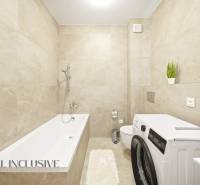 Világos csempékkel, káddal, mosógéppel és dekoratív növényekkel ellátott fürdőszoba egy négy szobás lakásban.