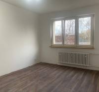 Szoba fehér falakkal, fa dekoros padlóval és nagy ablakkal egy kétszobás lakásban.
