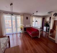 Egy szobás lakás belső tere fa padlóval, konyhával, világos függönyökkel és kényelmes ülőhellyel.