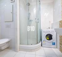 Fürdőszoba egy egyszobás lakásban mosógéppel, zuhanyzóval és kerámia csempékkel.