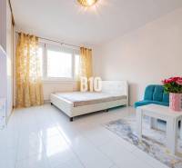 Világos szoba egy egyszobás lakásban kanapéval, asztallal és vázában lévő virágokkal.