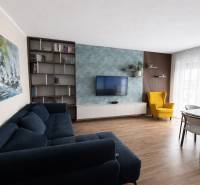 Nappali kék kanapéval, sárga fotellel és fa dekoros padlóval egy háromszobás lakásban.