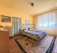 Hálószoba családi házban, fa dekoros padlóval, nagy ablakkal és szőnyegekkel.