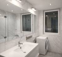 Fürdőszoba egy kétszobás lakásban káddal, mosdóval és mosógéppel, márvány kinézetű burkolattal.