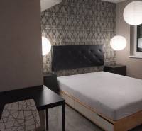 Hálószoba ággyal, esti világítás, asztal és szék egy kétszobás lakásban.