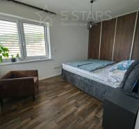 Hálószoba családi házban ággyal, székkel és fa mintázatú padlóval.