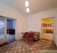 Családi ház belső tere fotelekkel, mosdóval, konyhával és két nyitott ajtóval.