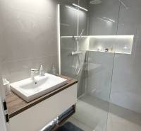 Fürdőszoba mosdóval, üveg zuhanykabinnal és világos csempékkel egy kétszobás lakásban.