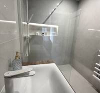 Fürdőszoba zuhanyzóval és mosdóval egy kétszobás lakásban, fa dekoros padlóval.