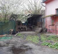 Kültér a gasztronómiai helyiségekben Búcsban, régi kemencével és tavaszi növényzettel.