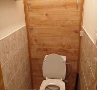 Csempeburkolatú falú és fa dekoros ajtajú WC egy kétszobás lakásban.