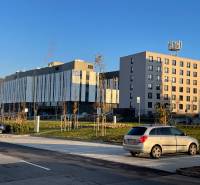 Épületek a Dominika utcában, Lamačban, Pozsonyban, parkolóval körülvéve és dombokkal a háttérben.