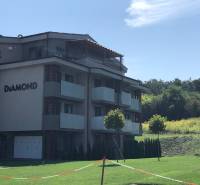 Kétszobás lakás épülete Podhájska településen, zölddel körülvéve és felhőtlen égbolttal.