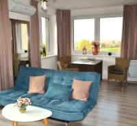 Nappali kanapéval, asztallal, növényekkel és fa dekorációjú padlóval egy kétszobás lakásban.