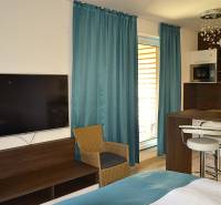 Garzonlakás TV-vel, fa bútorokkal, konyhapulttal és türkiz függönyökkel.