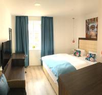 Világos szoba egy 2 szobás lakásban kék függönyökkel és fa mintázatú padlóval.