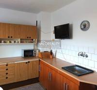 Konyha egy családi házban fa konyhabútorral, mikrohullámú sütővel és falra szerelt televízióval.