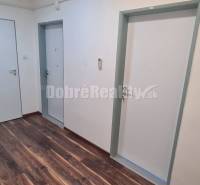 Irodák fehér falakkal, két ajtóval és fa mintázatú padlóval.