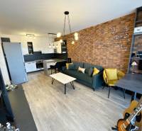 2 szobás lakás nappali része téglafallal, fa dekoros padlóval és konyhasarokkal.