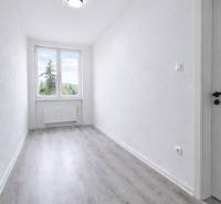 Keskeny szoba nagy ablakkal és fa dekorációjú padlóval egy háromszobás lakásban.