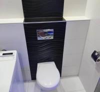Fürdőszoba egy háromszobás lakásban WC-vel és mosógéppel, fekete csempékkel.