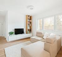 Világos nappali egy négy szobás lakásban, fa mintázatú padlóval, kanapéval és TV-vel.