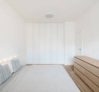 Világos hálószoba egy négy szobás lakásban, ággyal, párnákkal és szekrénnyel, fa dekoros padlóval.