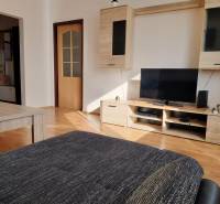 Nappali egy háromszobás lakásban fa dekor padlóval, televízióval és bútorokkal.