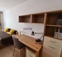 Íróasztal polcokkal, ágy és fa dekorációjú padló a kétszobás lakásban.