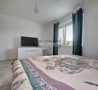 Hálószoba családi házban ággyal, televízióval és sötét függönyös ablakkal.