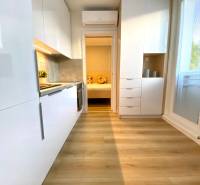 Világos konyha egy kétszobás lakásban, fa hatású padlóval és fehér szekrényekkel.