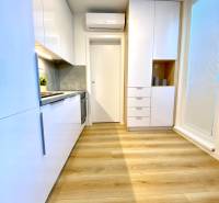 Konyha fehér szekrényekkel és fa dekor padlóval egy kétszobás lakásban.