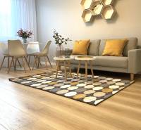 2 szobás lakás fa mintázatú padlóval, kanapéval, étkezőasztallal és geometrikus polcokkal.