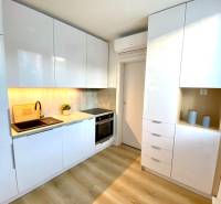 Konyha egy kétszobás lakásban fehér szekrényekkel és fa mintázatú padlóval.