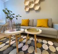 Nappali egy kétszobás lakásban geometrikus polcokkal, szürke kanapéval és színes szőnyeggel.