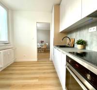 Konyha egy kétszobás lakásban fehér szekrényekkel és fa mintázatú padlóval.