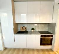 Konyha fehér szekrényekkel, szürke munkalappal és fa mintázatú padlóval, 2 szobás lakás.