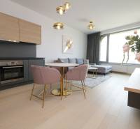 Nappali konyhával, fa mintázatú padlóval, világos kanapéval, étkezőasztallal, virágokkal.