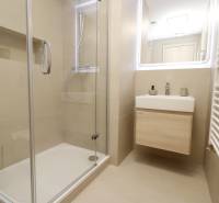 Fürdőszoba üveg zuhanykabinnal és világos mosdóval egy kétszobás lakásban.