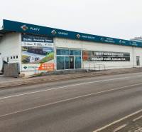 Üzlethelyiségek a Kő utcában, Zsolnán, reklámfeliratokkal és üres parkolóval.