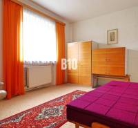 Szoba szőnyegpadlóval, krémszínű karosszékkel, színes ággyal és szekrénnyel egy családi házban.