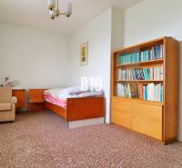 Szoba családi házban ággyal, könyvespolccal és szőnyegen lévő fotellel.