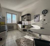 Konyha egy kétszobás lakásban fehér szekrényekkel, ablakkal és étkezőasztallal.