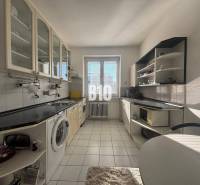 Konyha egy kétszobás lakásban fehér szekrényekkel és fekete munkalappal.