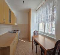 Konyha fa szekrényekkel, asztallal és két székkel egy háromszobás lakásban.