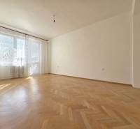 Tágas szoba nagy ablakokkal és fa dekorációjú padlóval egy háromszobás lakásban.