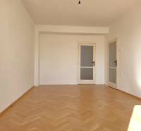 Egy szoba a háromszobás lakásban fa dekorációjú padlóval és fehér falakkal rendelkezik.