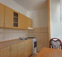 Konyha világos bútorokkal, tűzhellyel és asztallal egy háromszobás lakásban.